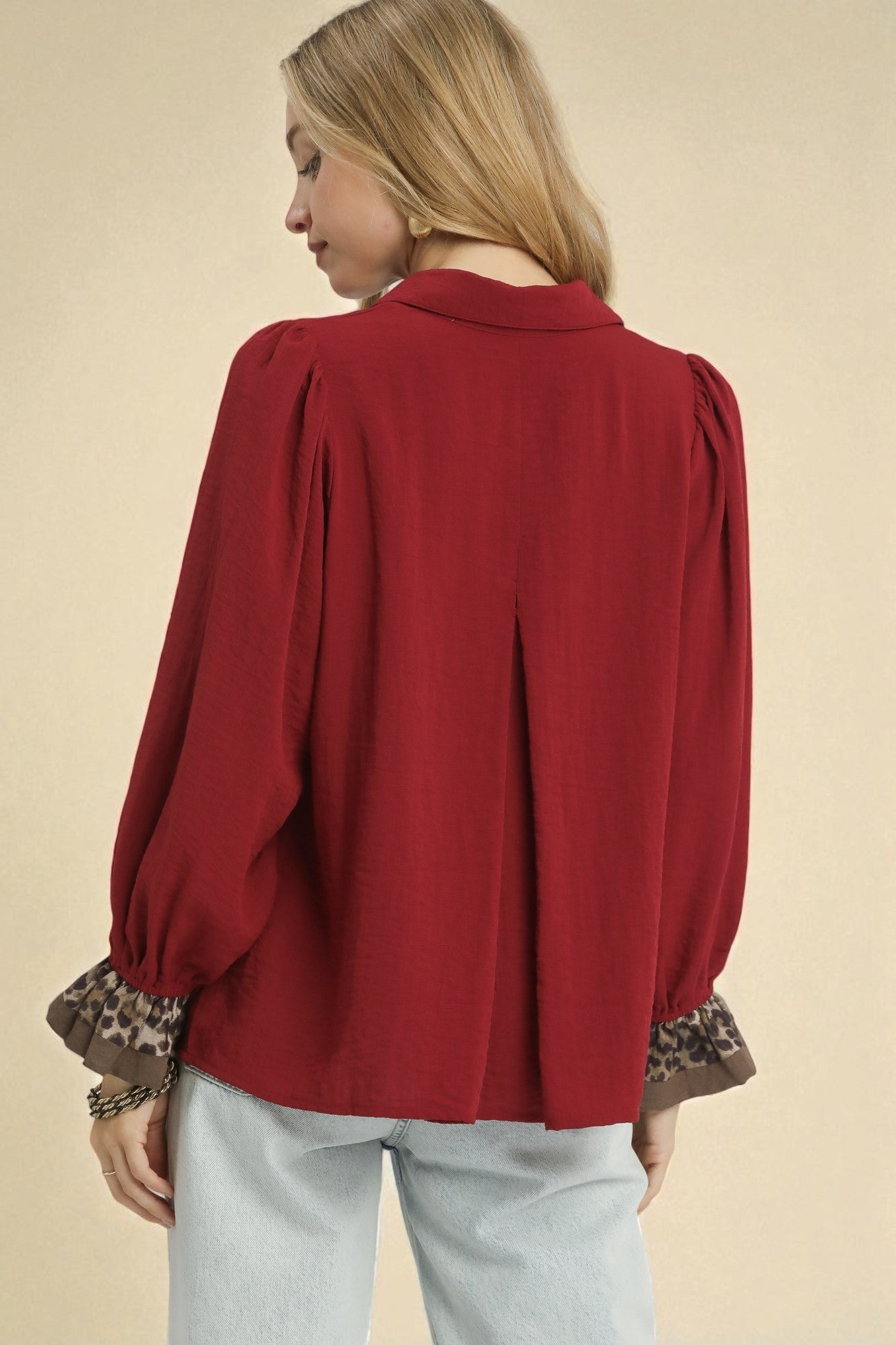 Red blouse with long sleeves and patterned cuffs worn by a person on a beige background