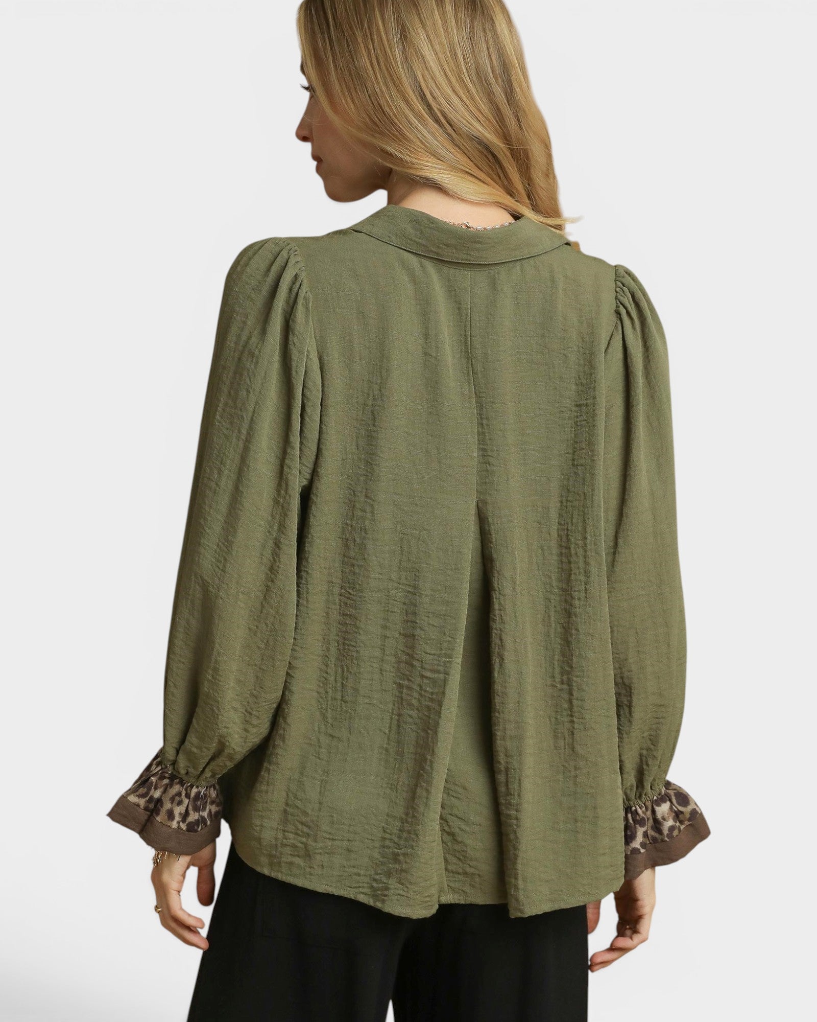 Woman wearing an olive green blouse with long sleeves and leopard print cuffs on a white background