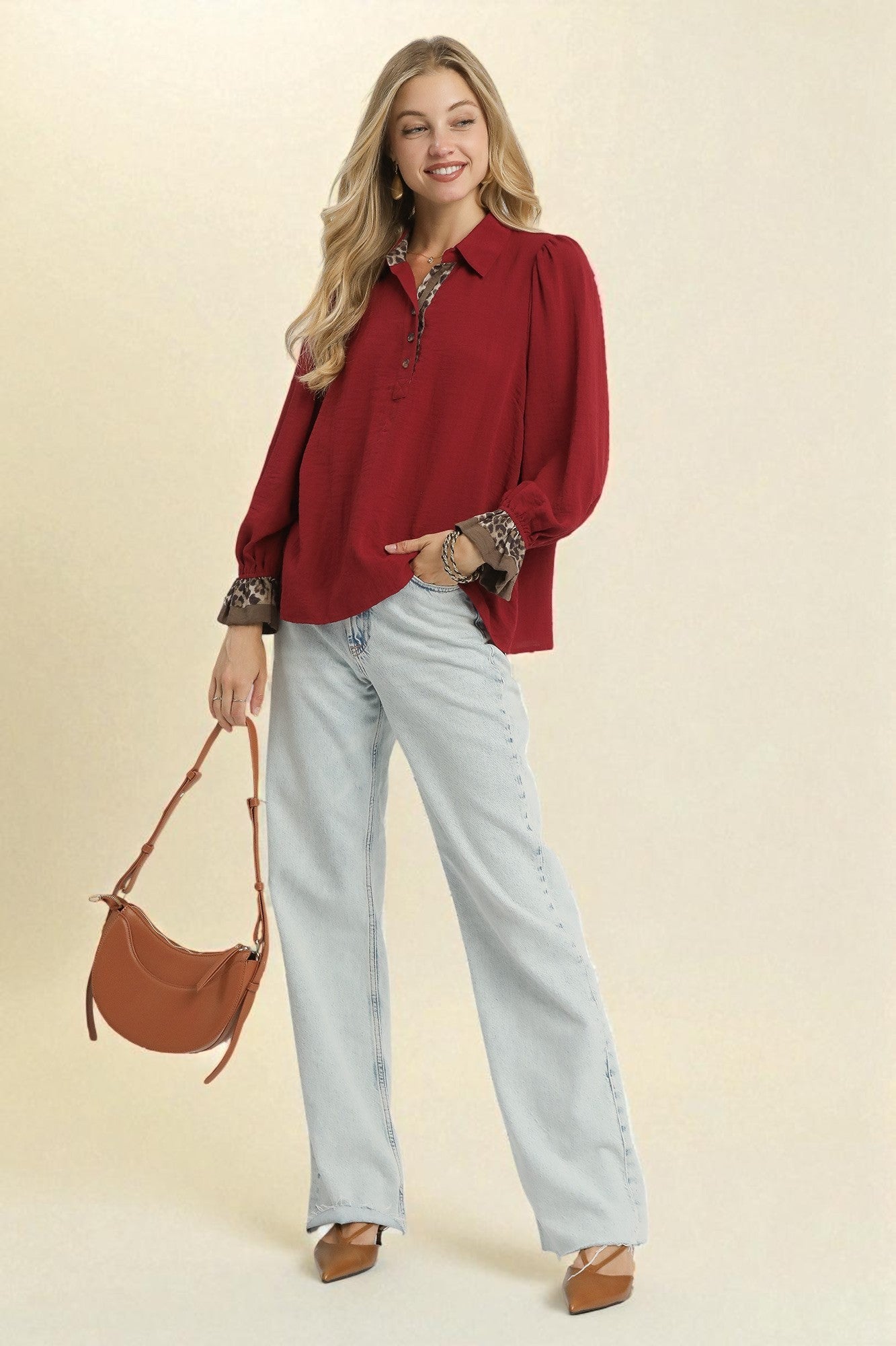 Woman wearing a red blouse and light blue jeans, holding a brown handbag on a beige background
