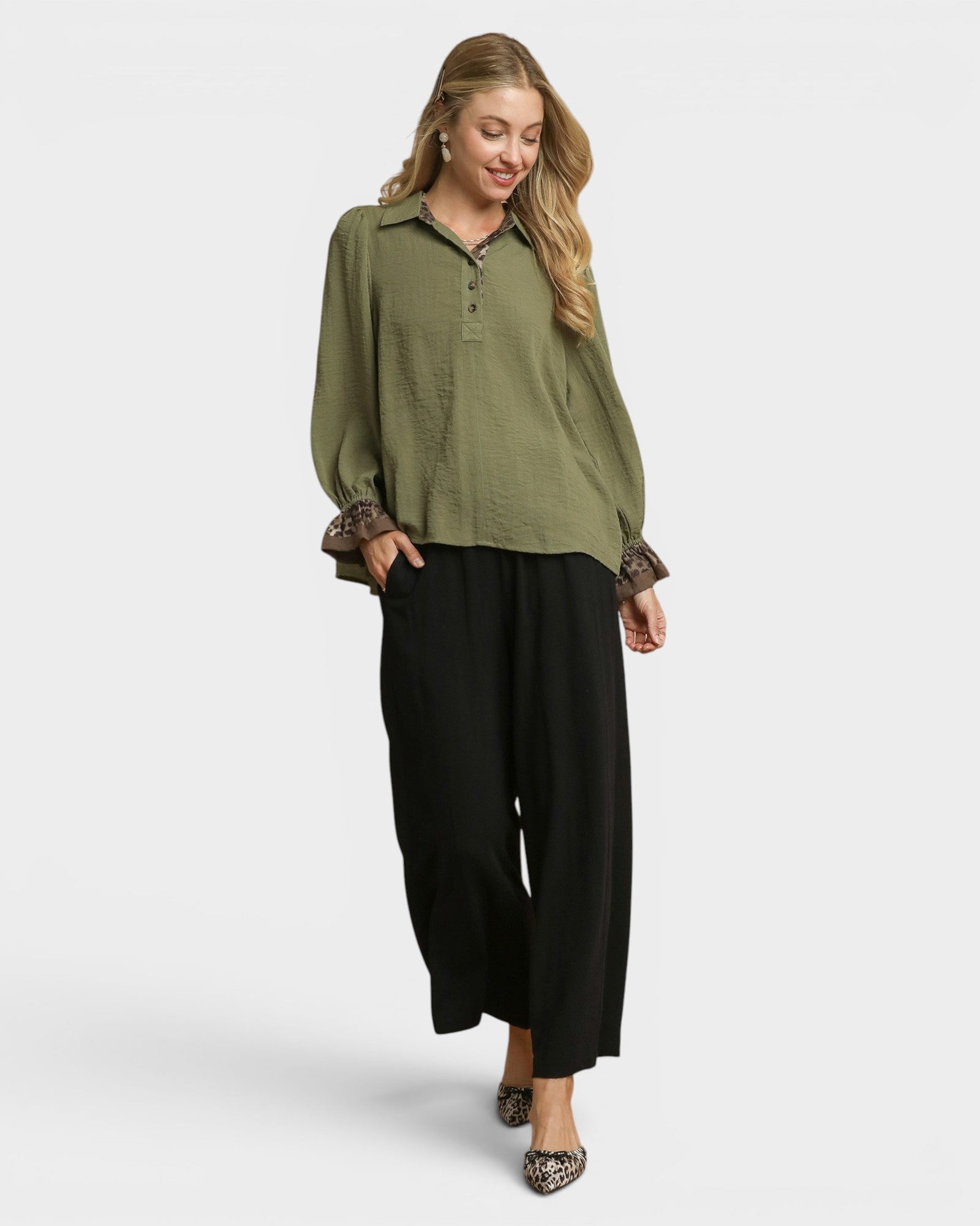 Woman wearing an olive green blouse with a patterned sleeve and black pants on a white background