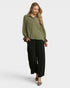 Woman wearing an olive green blouse with a patterned sleeve and black pants on a white background