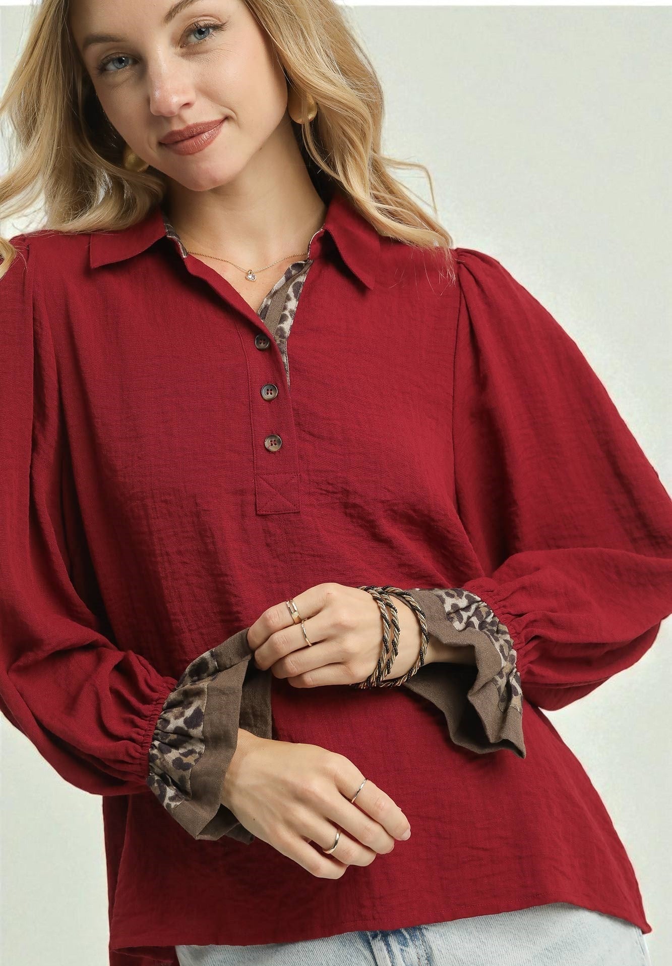 Woman wearing a burgundy blouse with patterned cuffs on a plain background