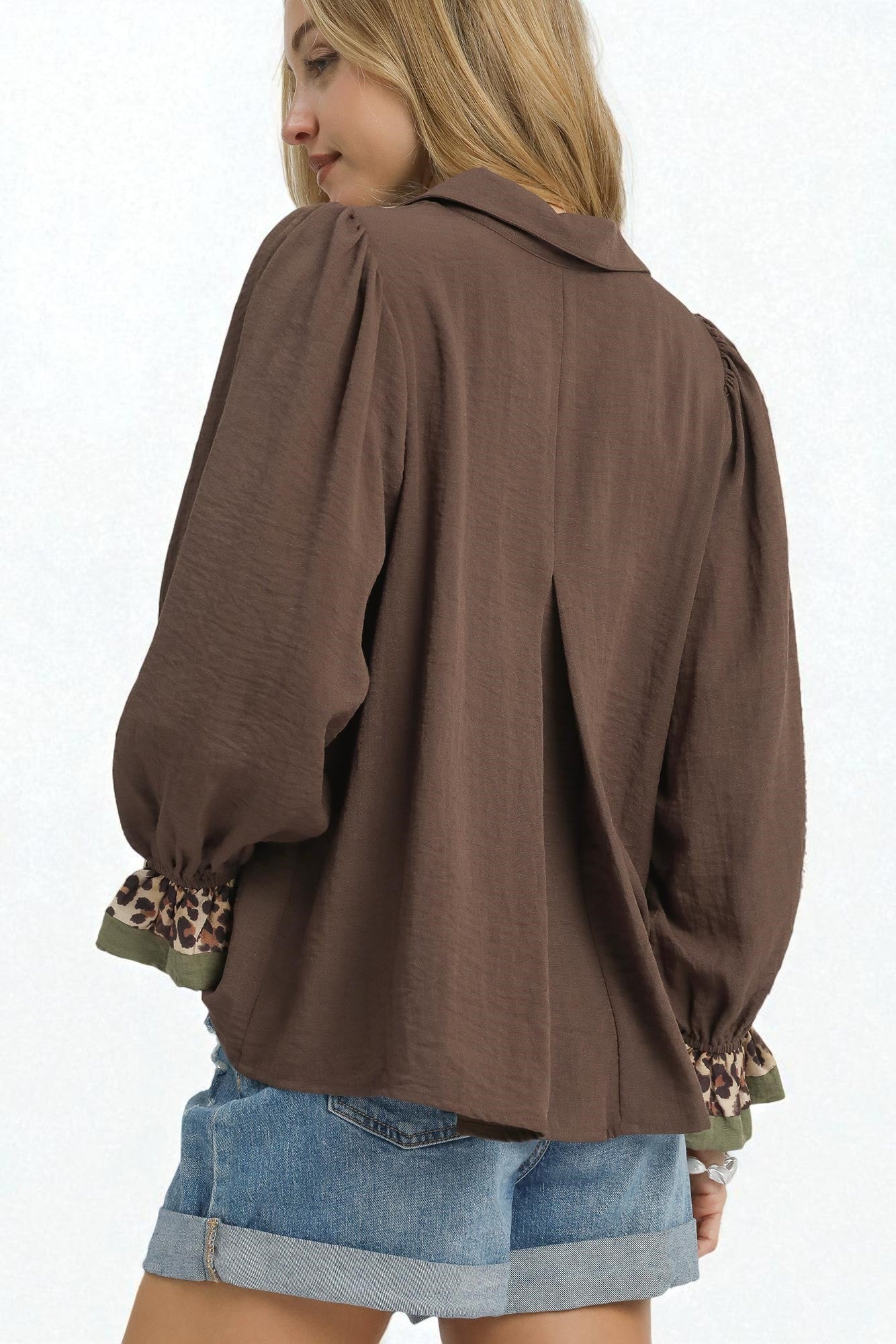 Woman wearing a brown blouse with leopard print cuffs on a white background