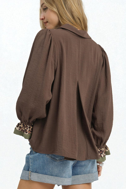 Woman wearing a brown blouse with leopard print cuffs on a white background