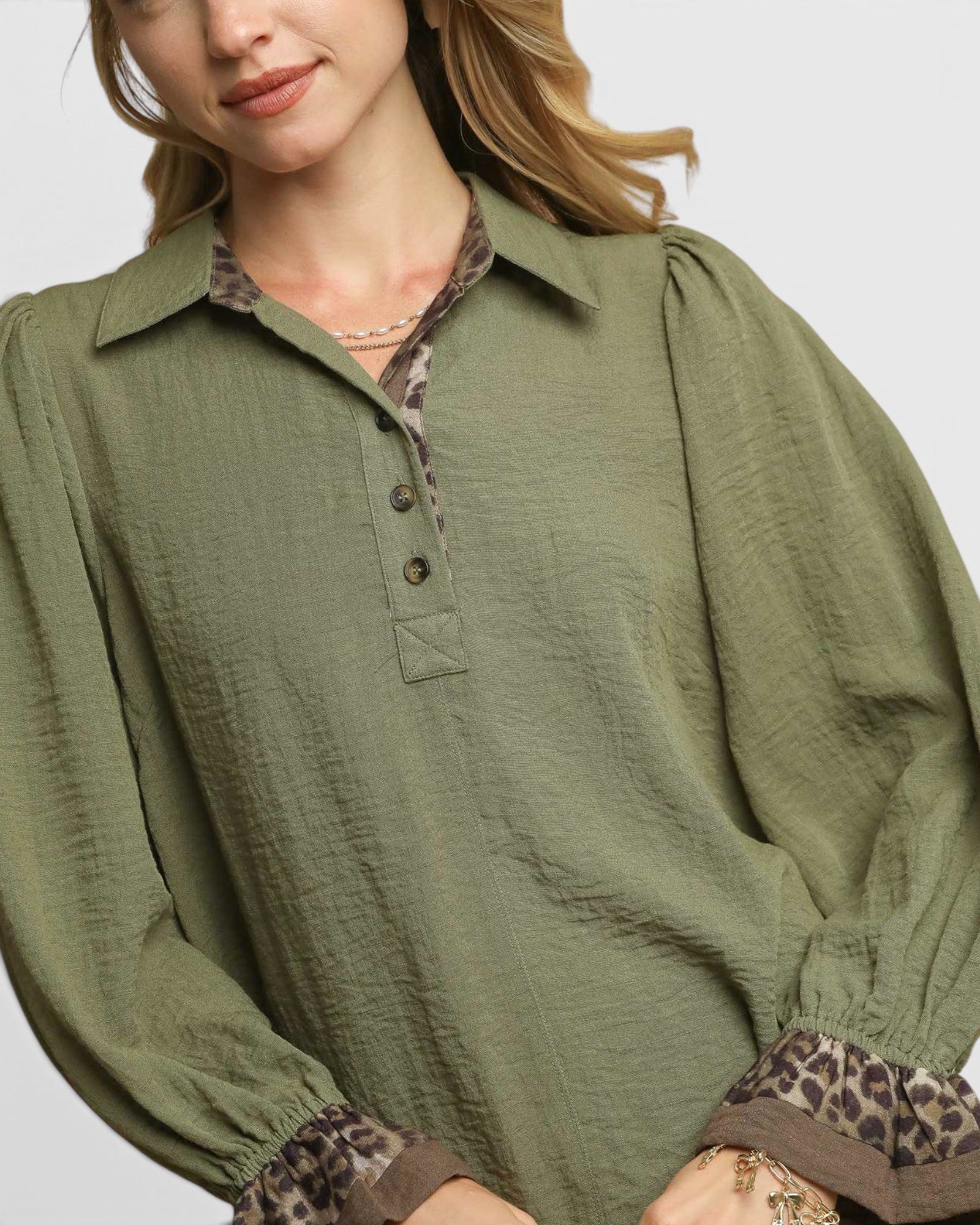 Woman wearing a green blouse with patterned cuffs on a plain background