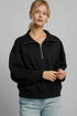 Woman wearing a black quarter-zip sweatshirt and light blue jeans against a gray background