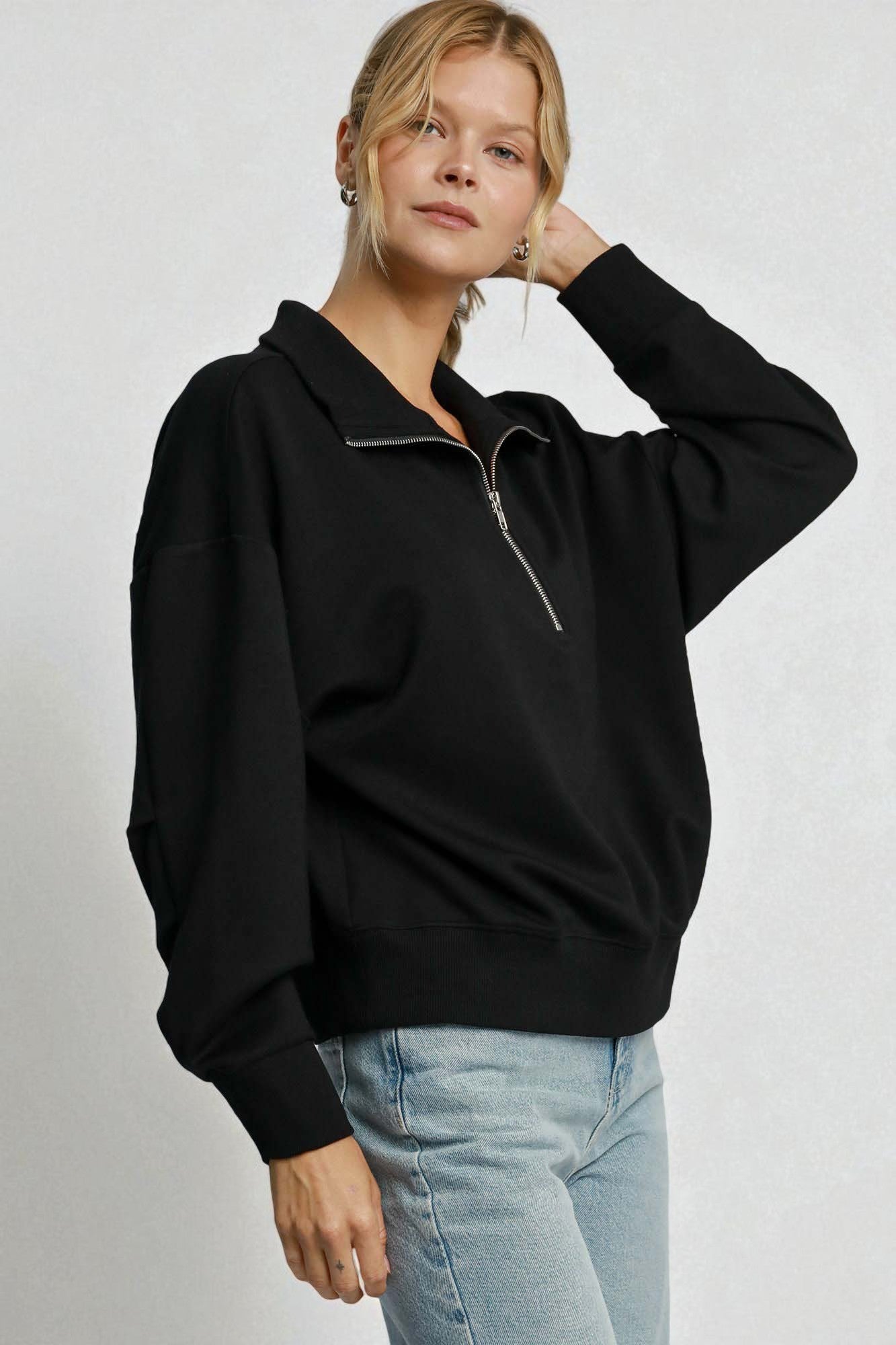 Person wearing a black sweater with a zipper on a plain background