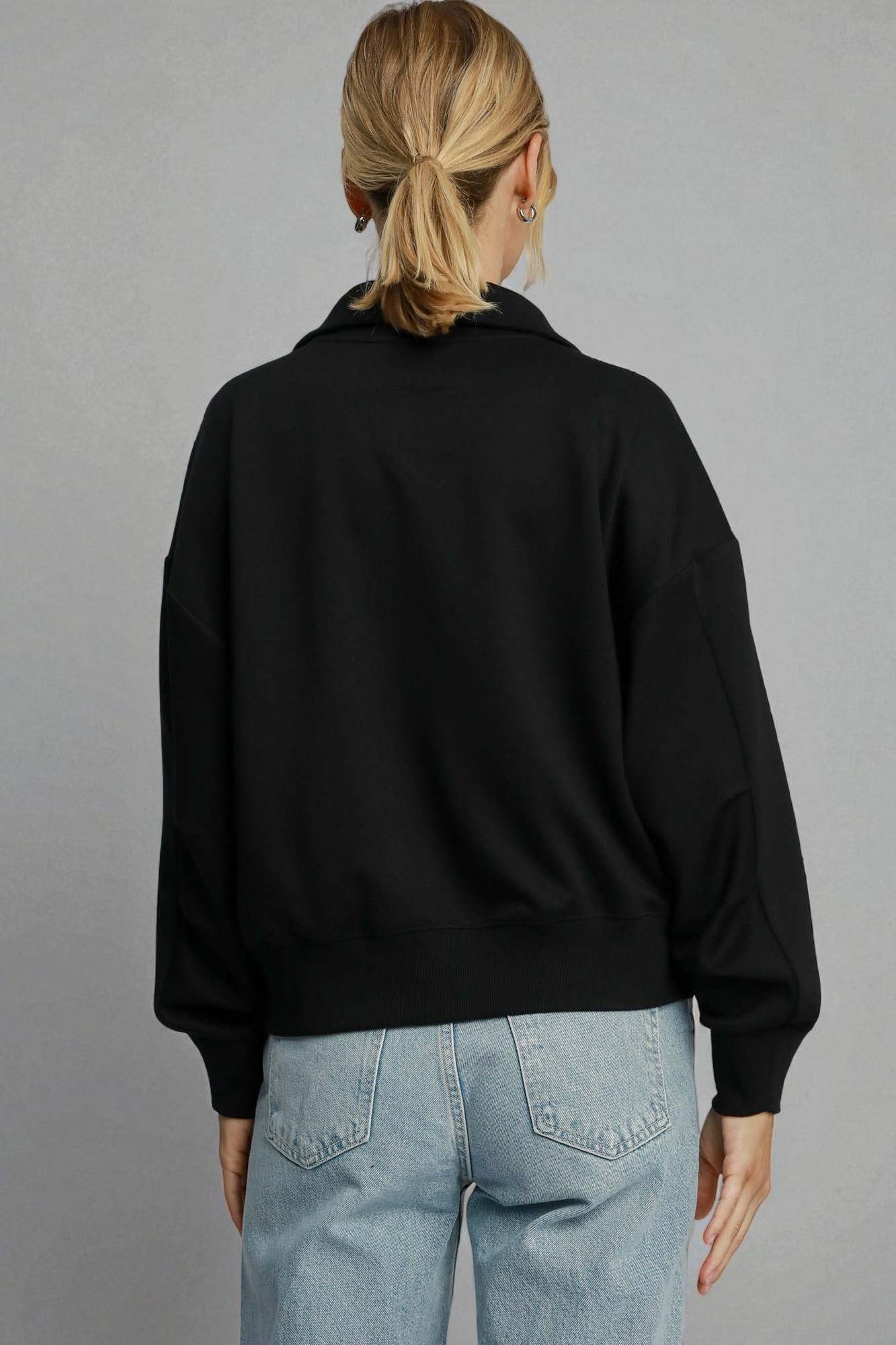 Person wearing a black jacket and light blue jeans on a gray background