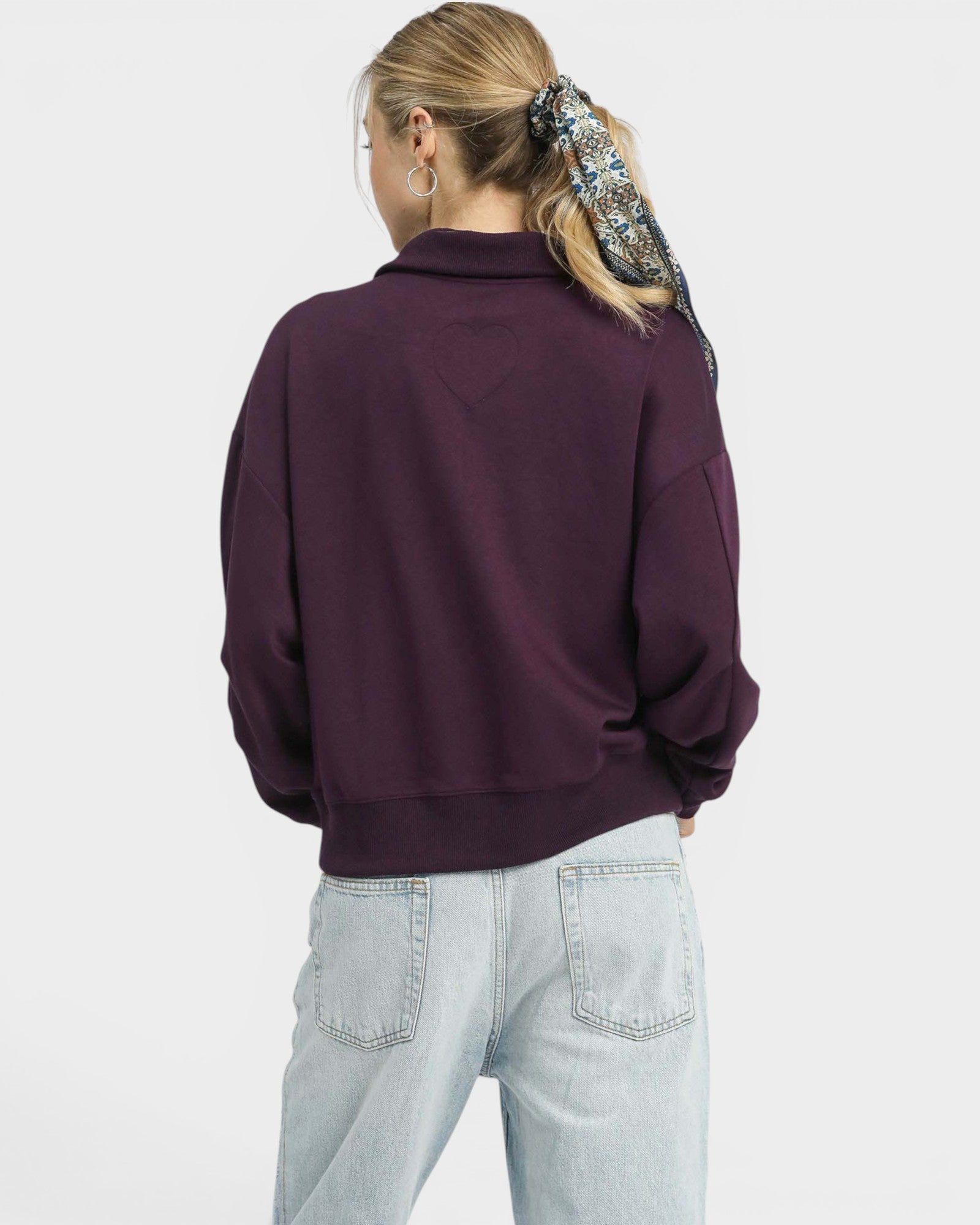 Person wearing a purple sweatshirt and light blue jeans on a white background