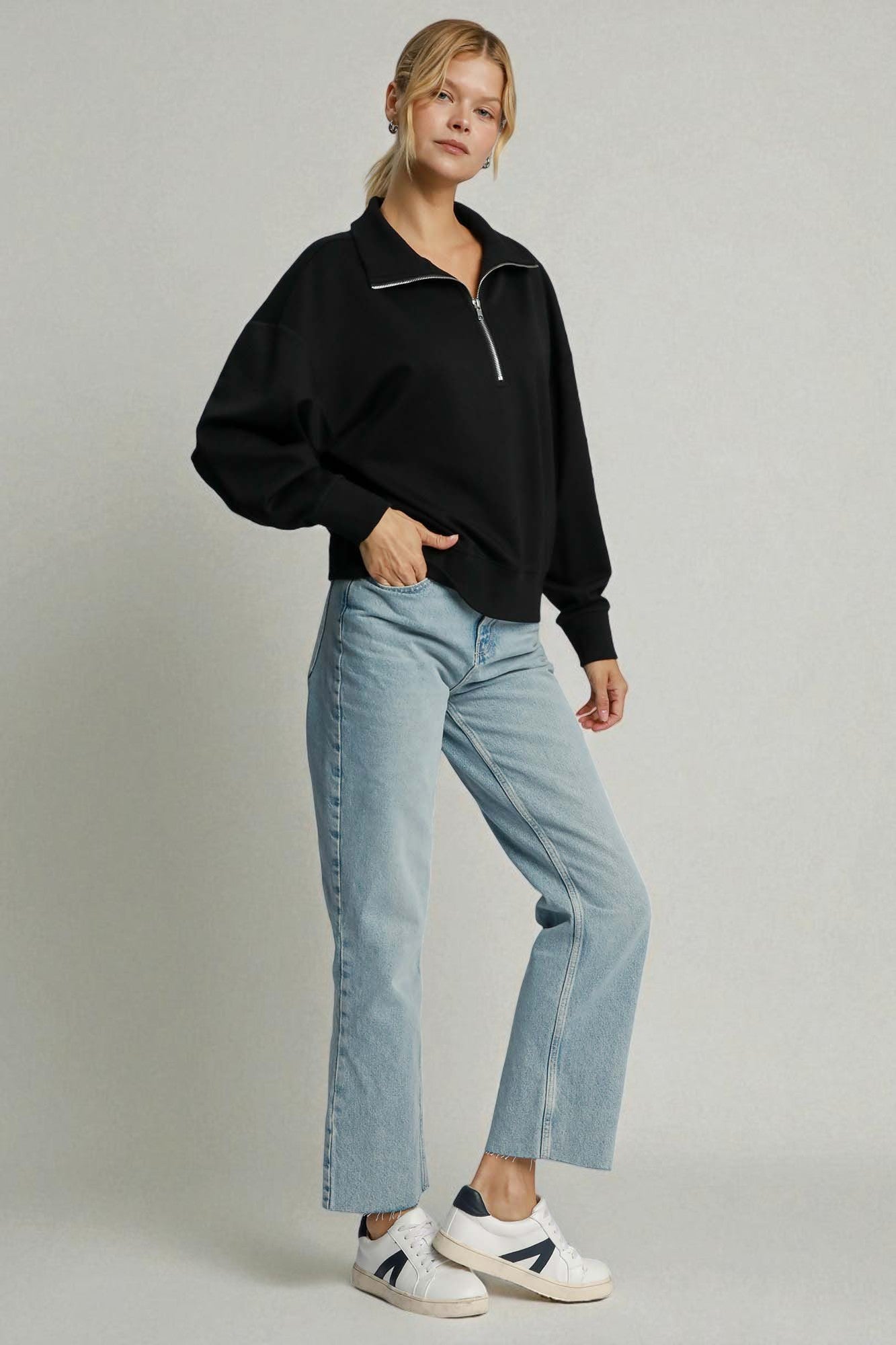 Person wearing a black sweater and light blue jeans on a plain background