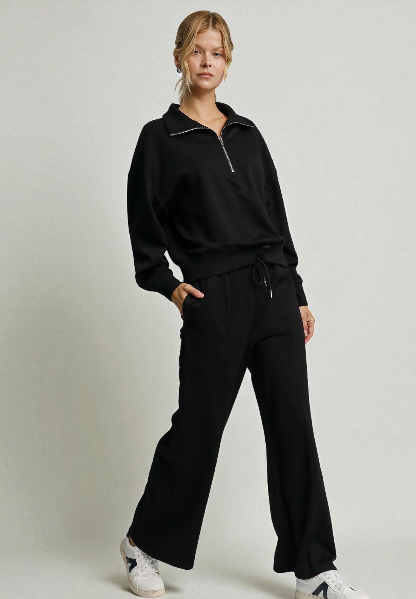 Person wearing a black outfit with white sneakers on a light gray background