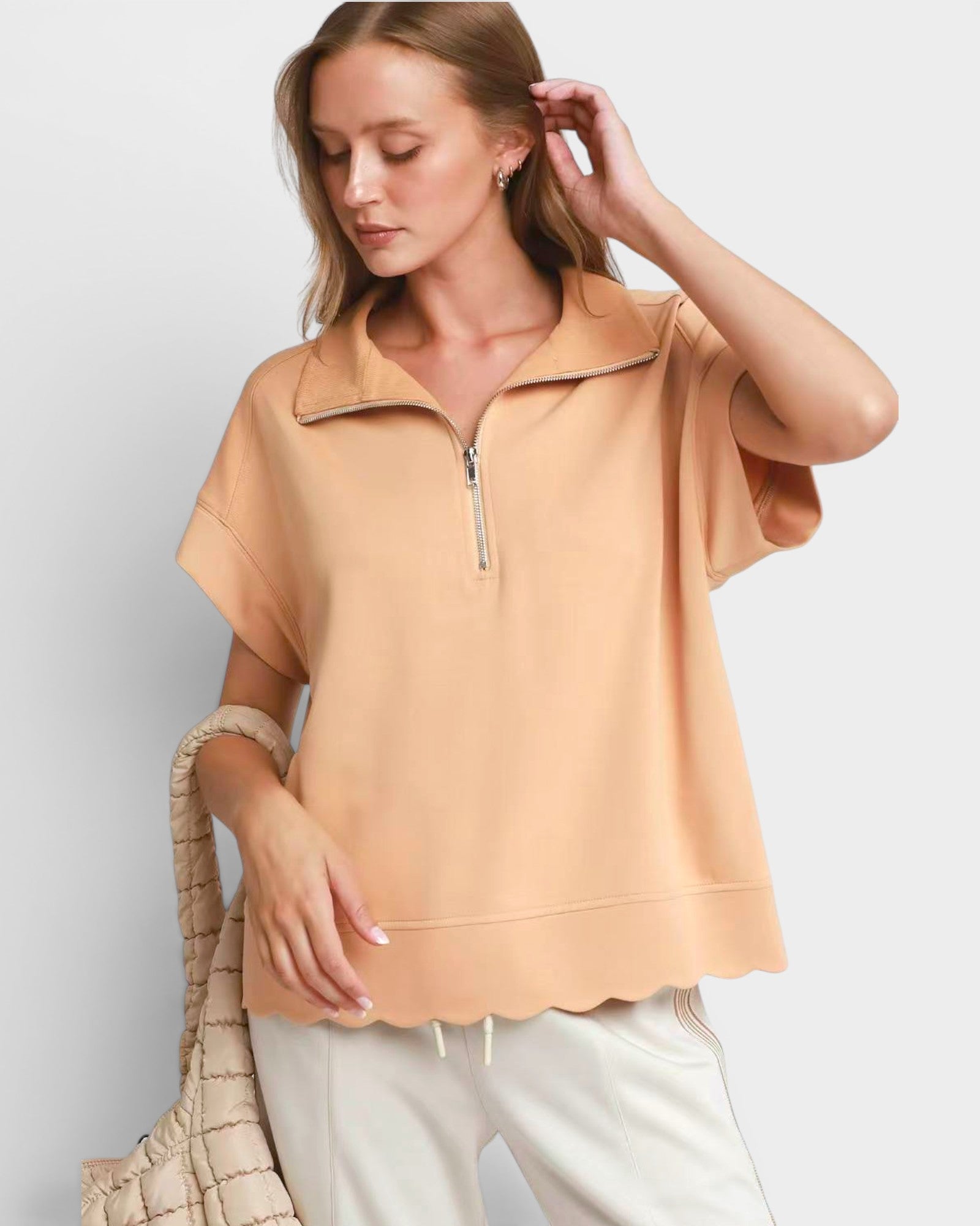 Woman wearing a beige short-sleeve top with a zipper on a light gray background