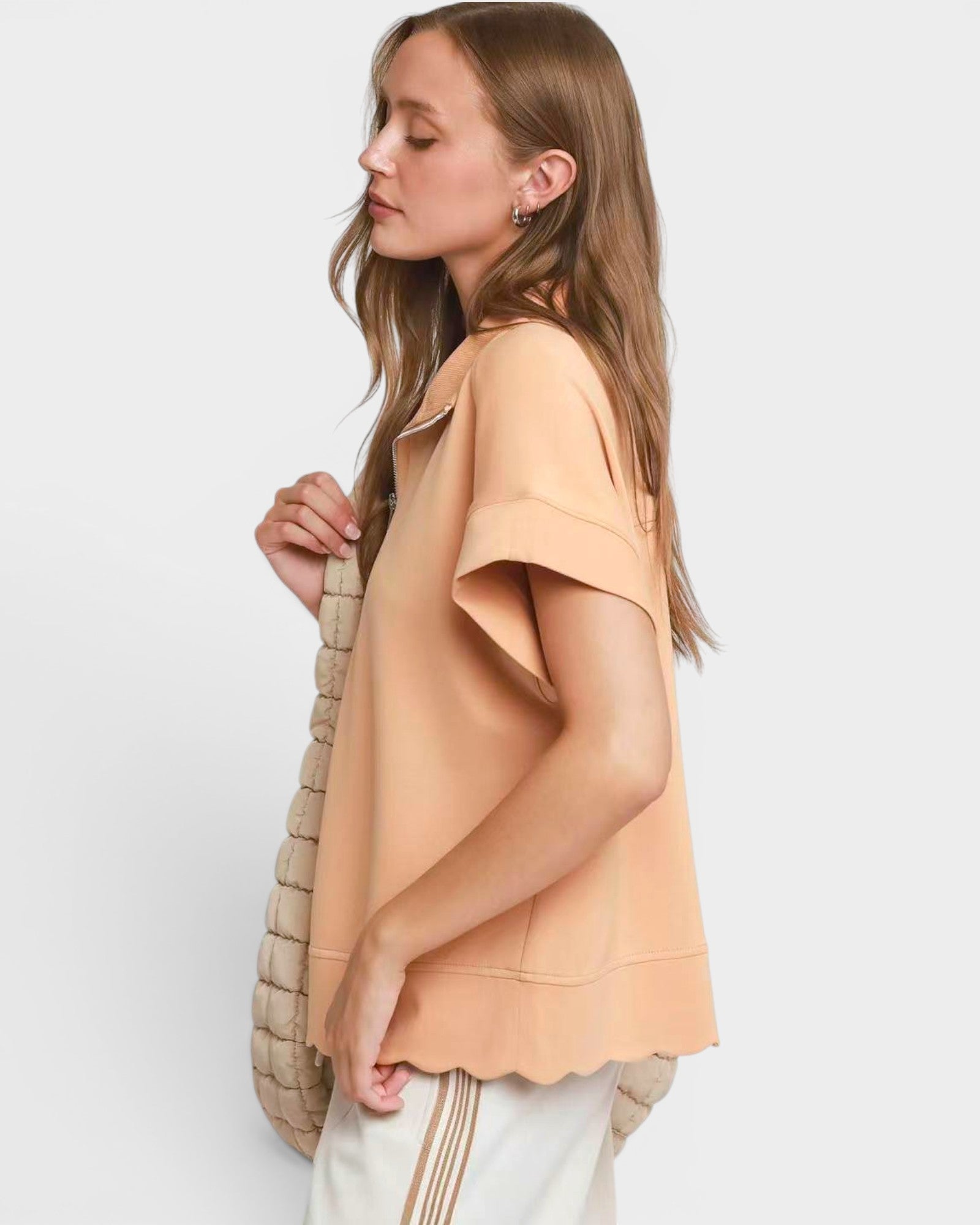Woman wearing a peach-colored top with a neutral bag on a light background