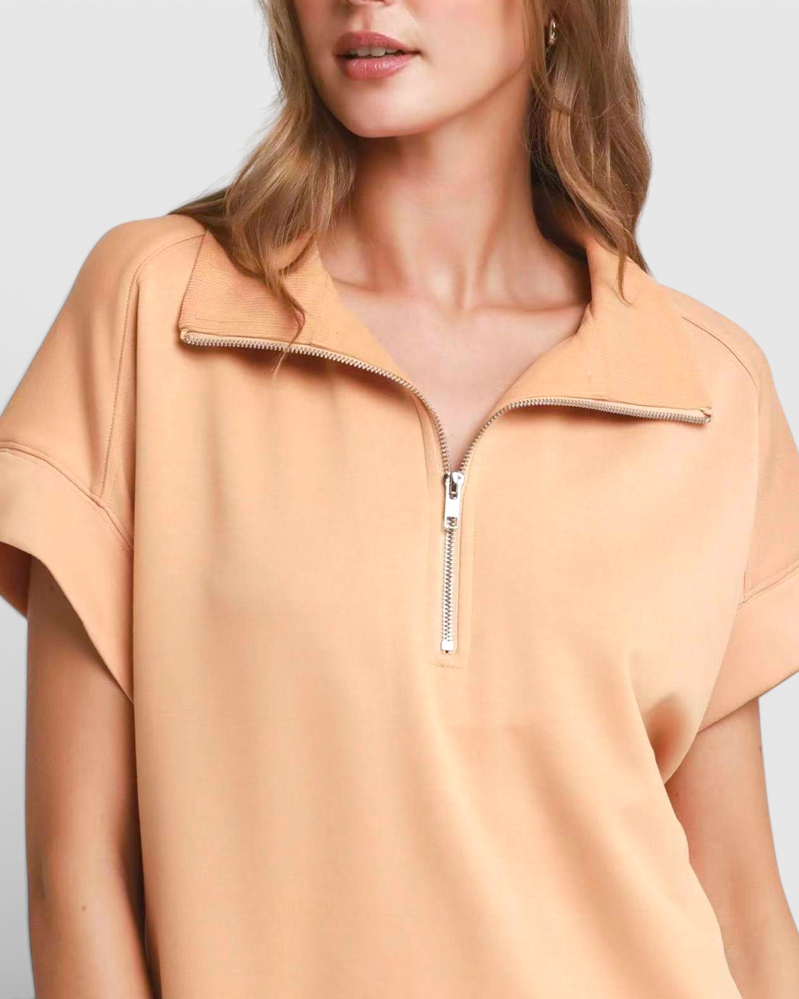 Woman wearing a beige short-sleeve top with a zipper detail on a light gray background