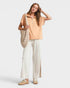 Woman wearing a beige top and white pants, holding a checkered bag on a light gray background