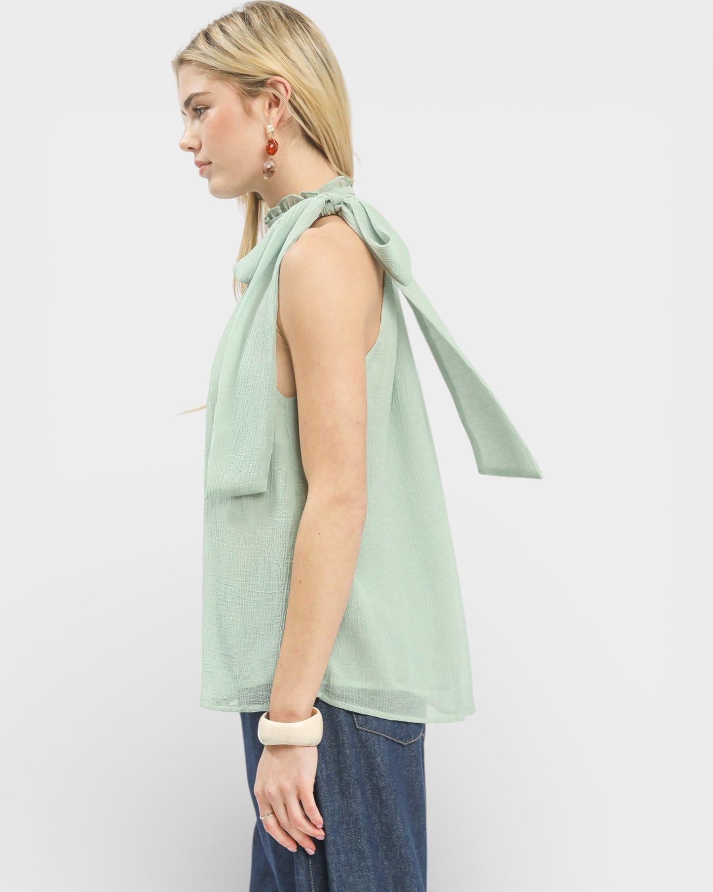 Woman wearing a light green sleeveless top with a bow detail on a white background