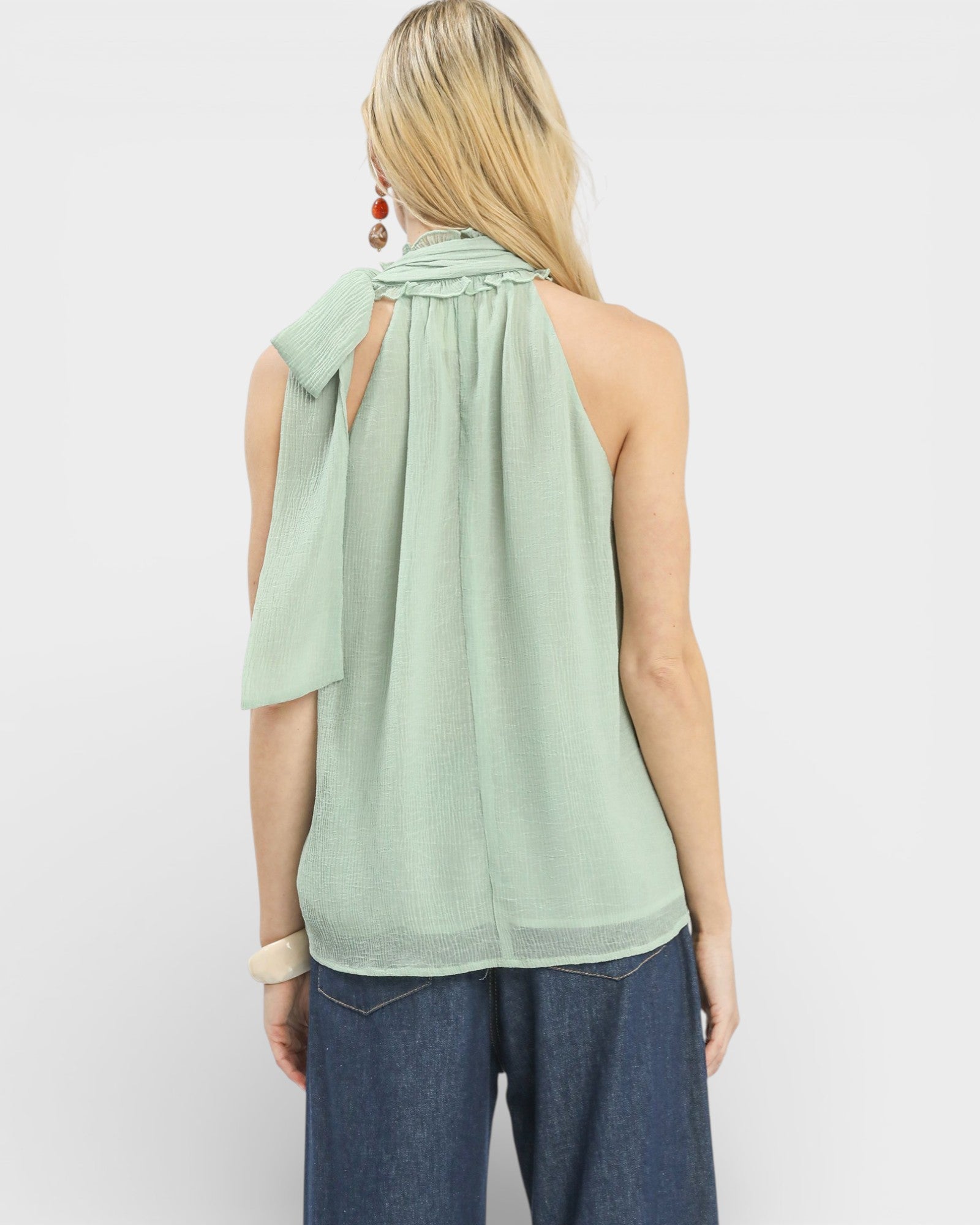 Person wearing a light green halter top and blue jeans on a white background