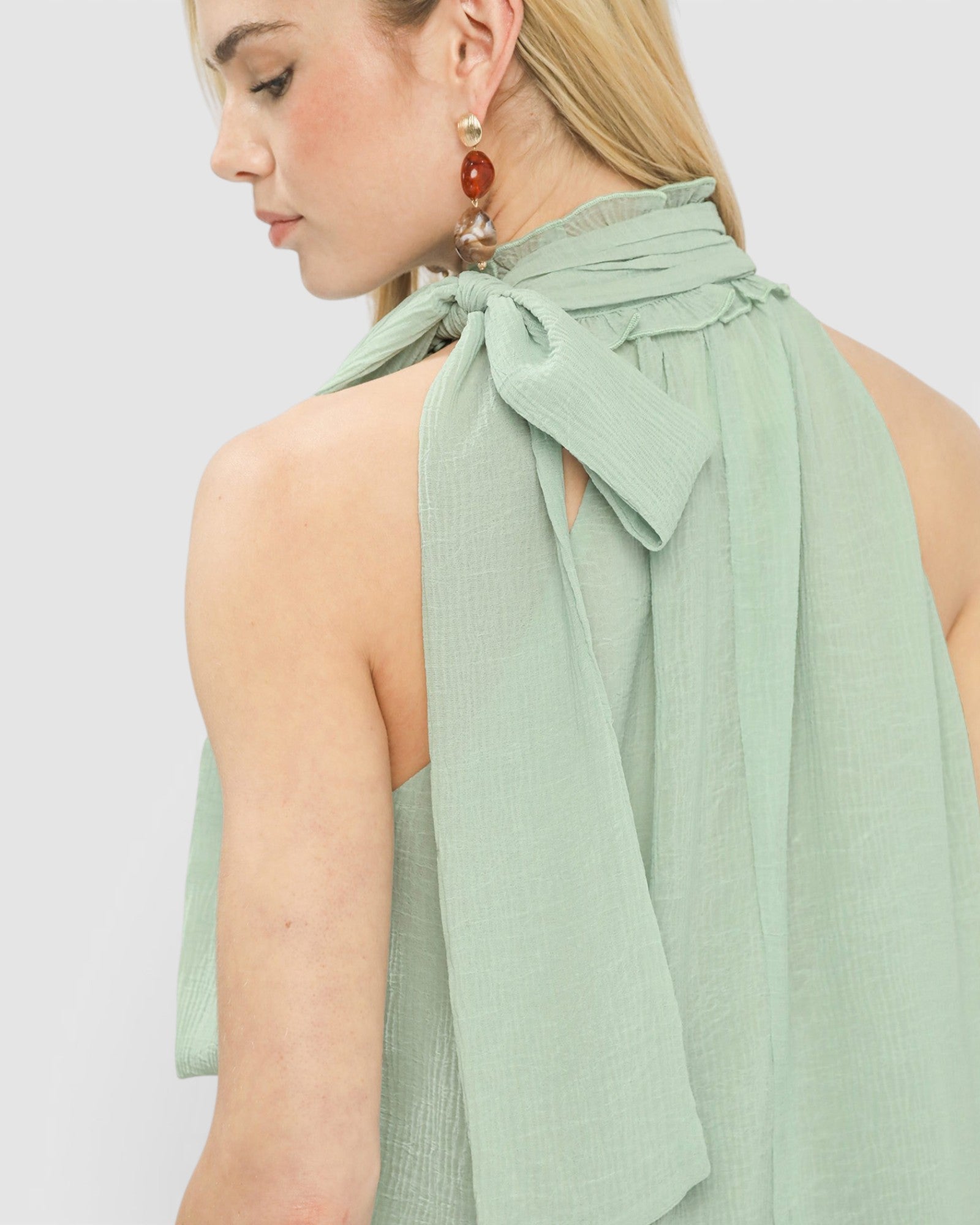 Woman wearing a light green halter top with a bow detail on a plain background