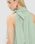 Woman wearing a light green halter top with a bow detail on a plain background