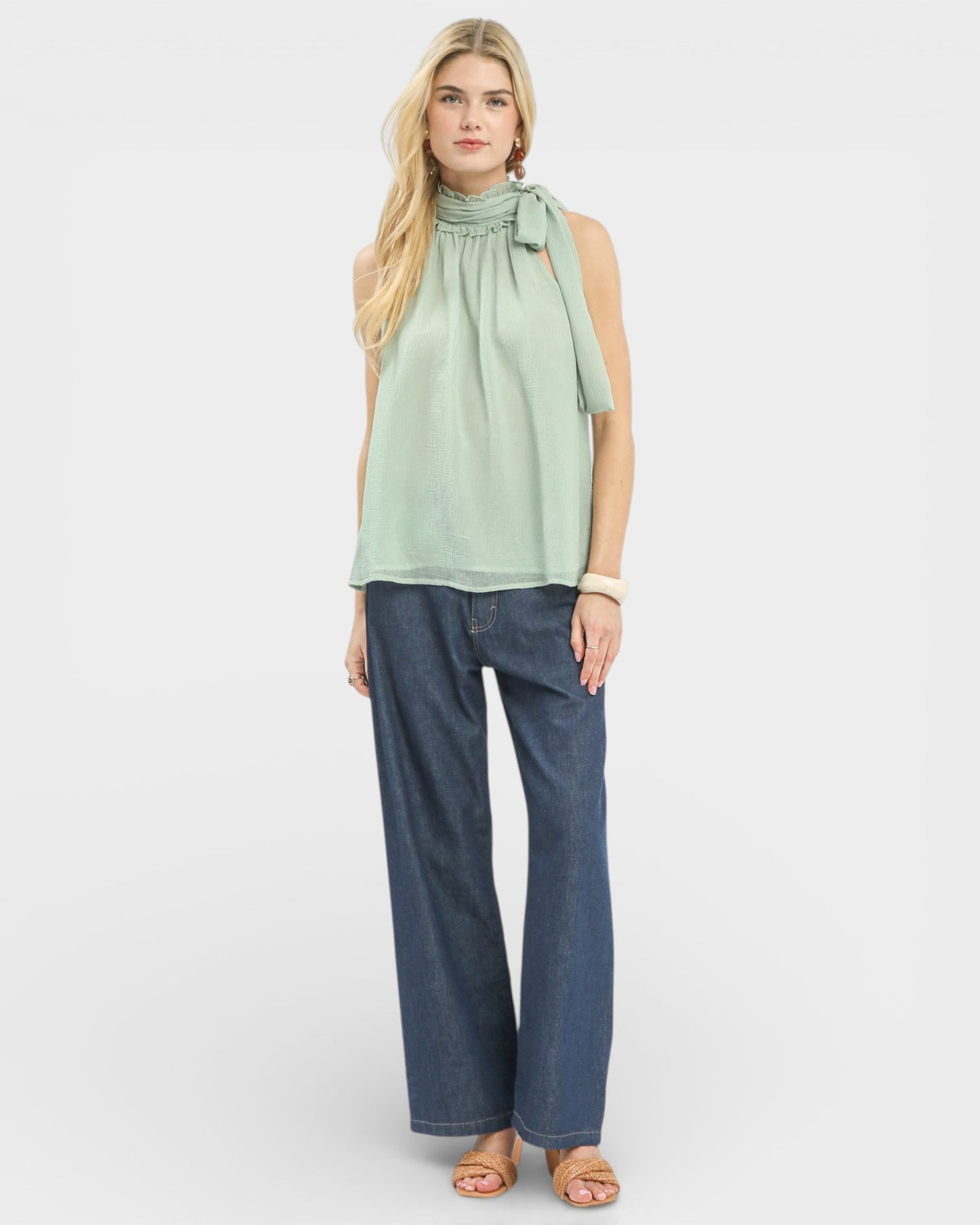 Woman wearing a light green top and blue jeans on a white background