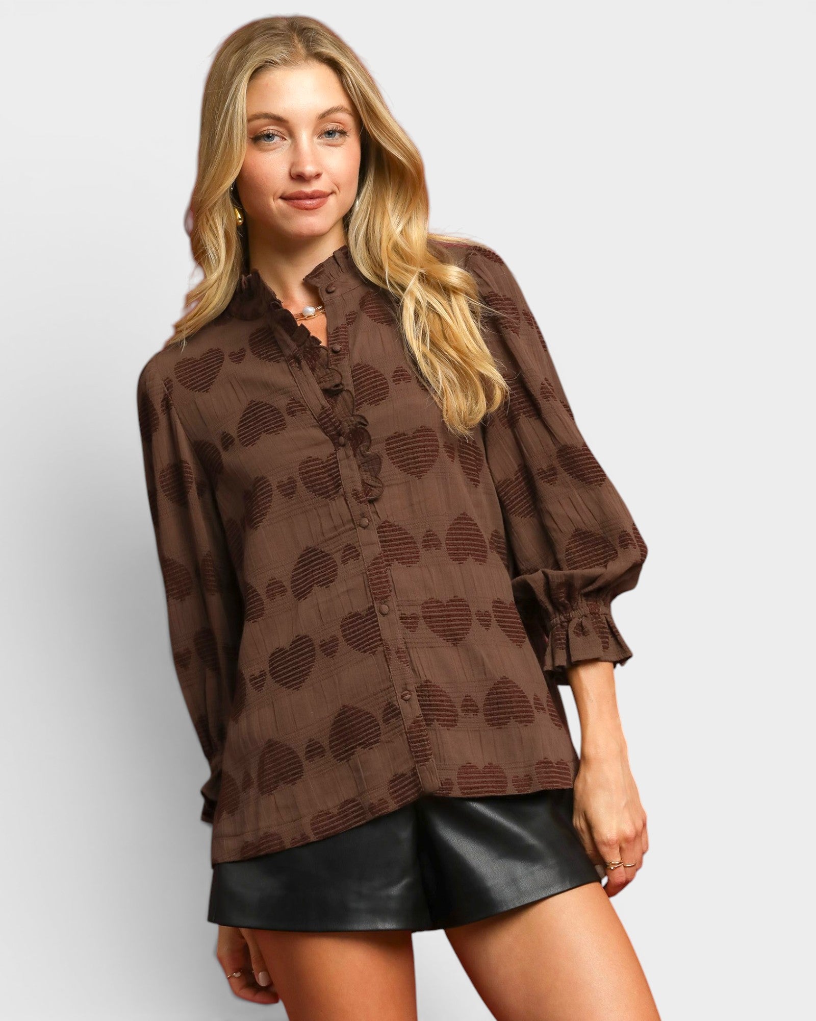 Woman wearing a brown patterned blouse and black shorts on a plain background