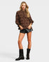 Woman wearing a brown patterned blouse, black leather shorts, and black boots on a white background
