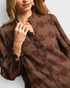 Woman wearing a brown patterned blouse with a blurred background