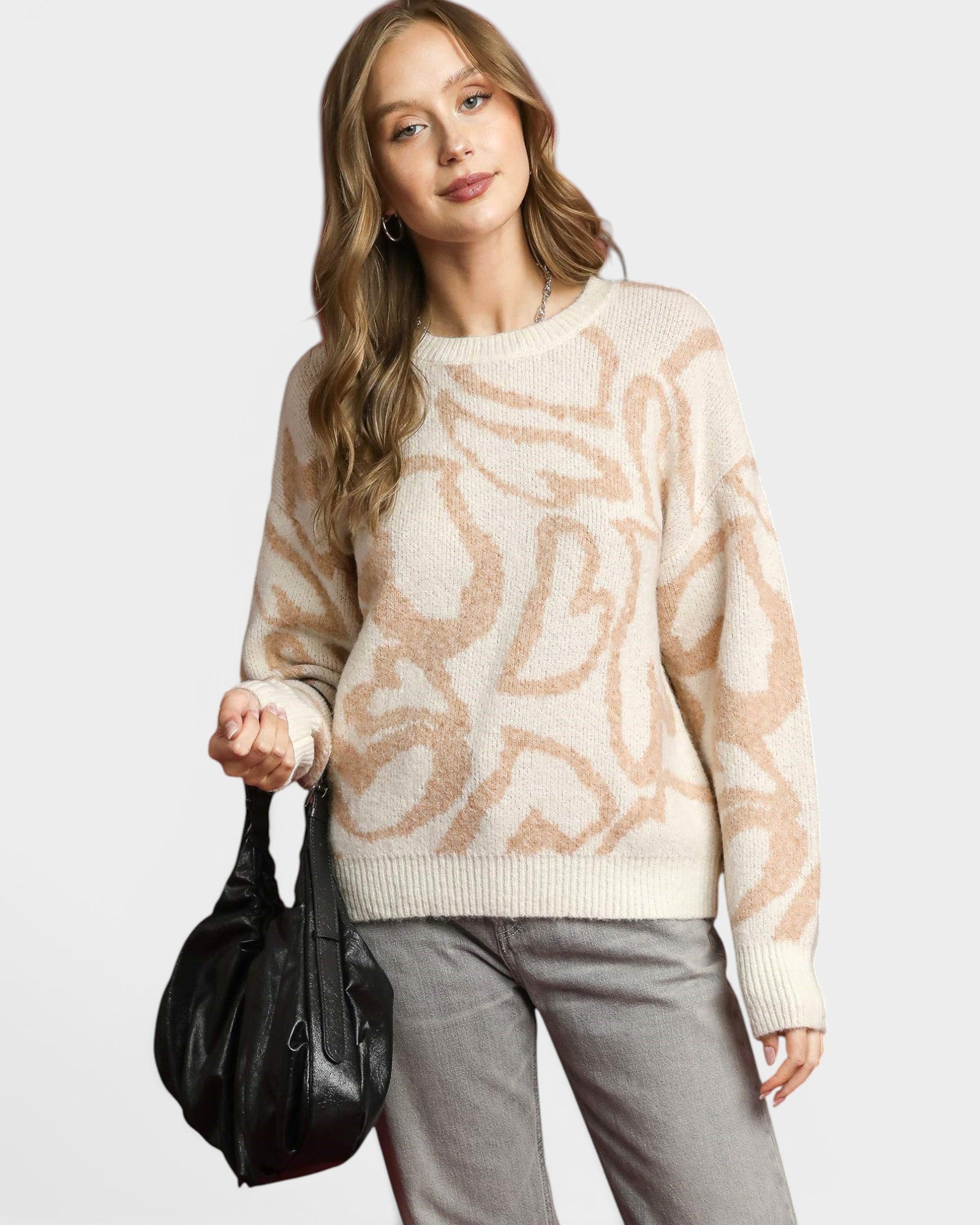 Woman wearing a patterned sweater holding a black handbag on a white background
