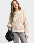 Woman wearing a patterned sweater holding a black handbag on a white background