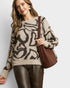 Woman wearing a patterned sweater holding a brown handbag against a plain background