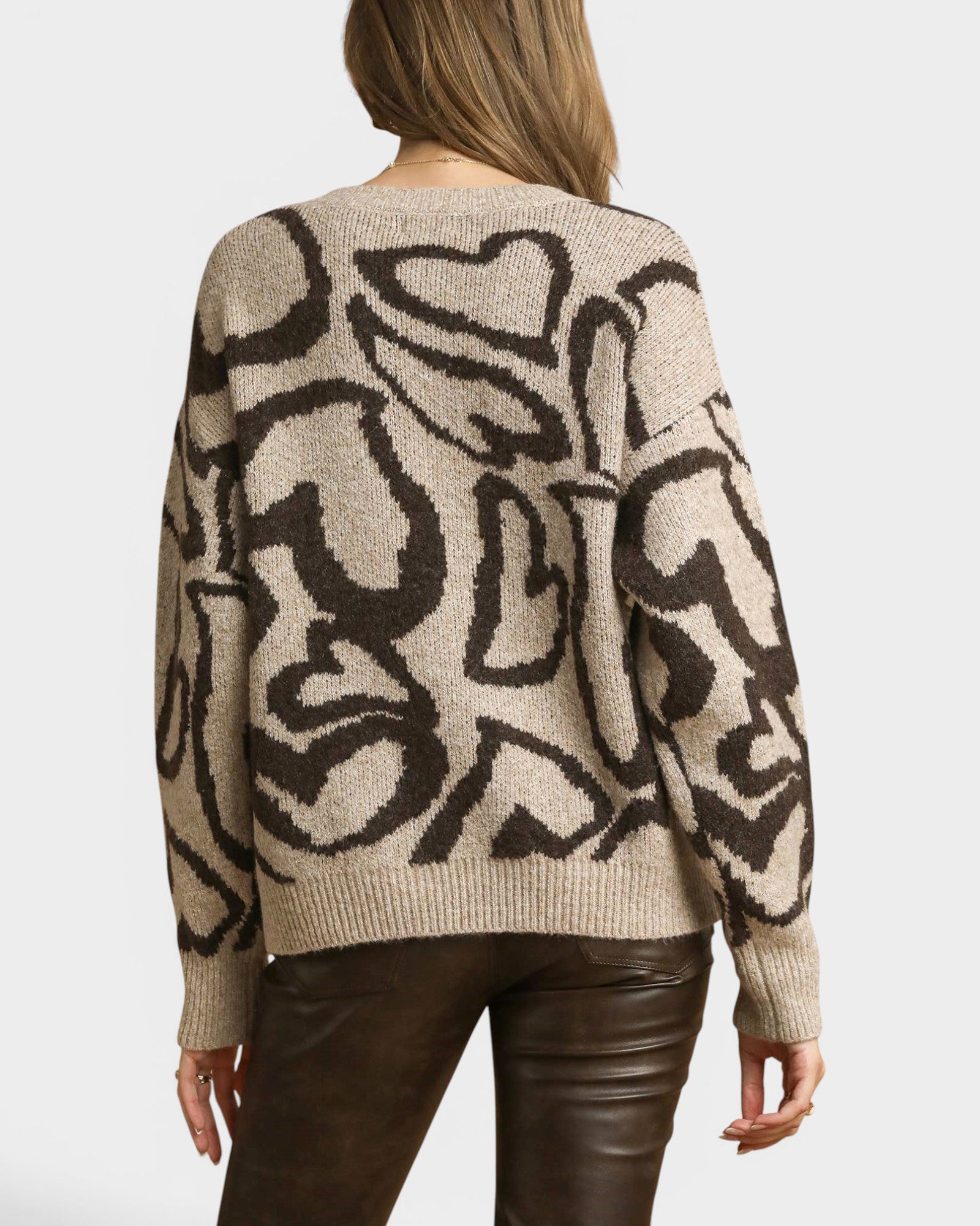 Beige sweater with black abstract patterns worn by a person on a plain background