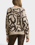 Beige sweater with black abstract patterns worn by a person on a plain background