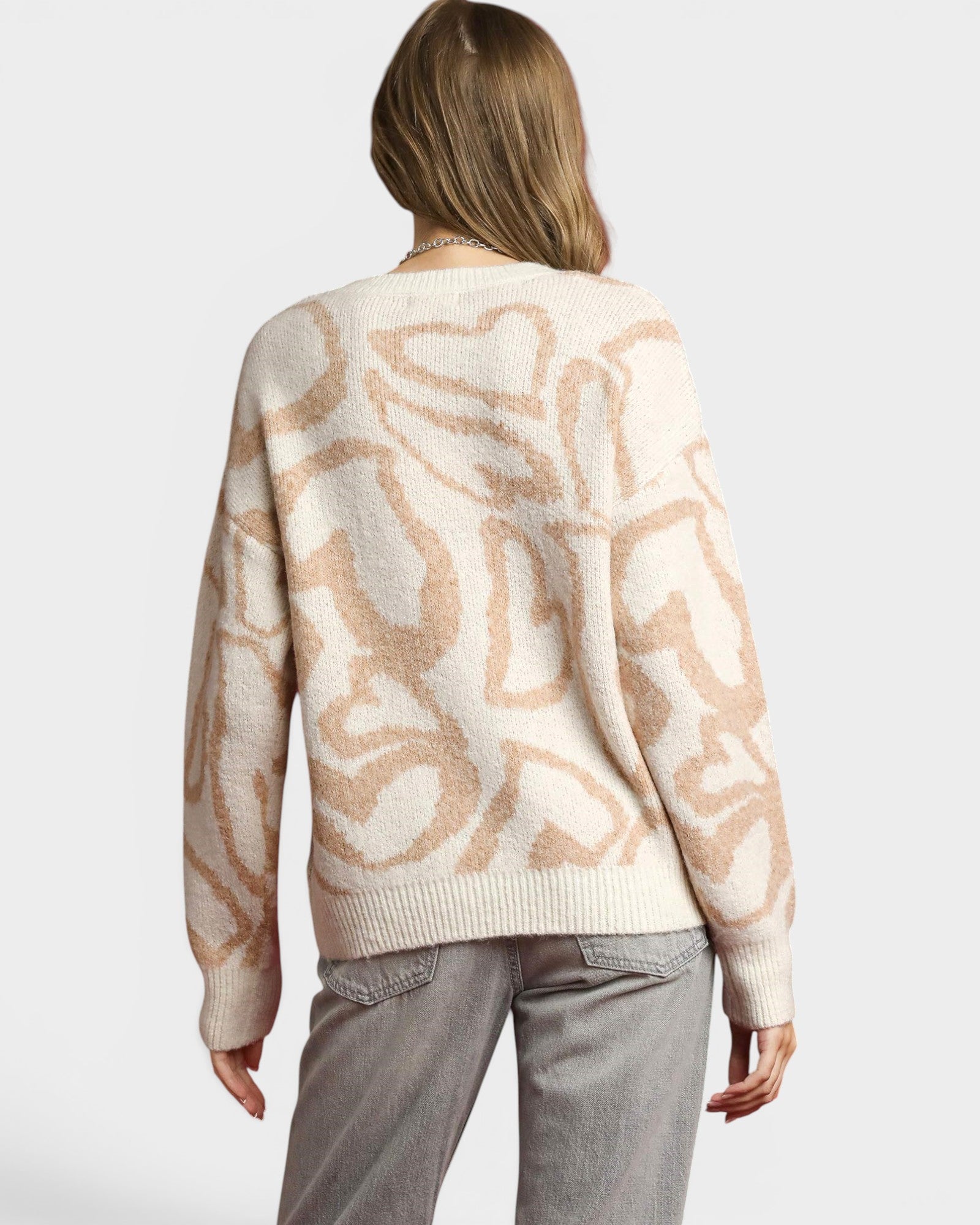 Person wearing a beige sweater with abstract pattern on a plain background
