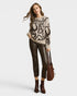 Woman wearing a patterned sweater and leather pants holding a brown bag on a white background