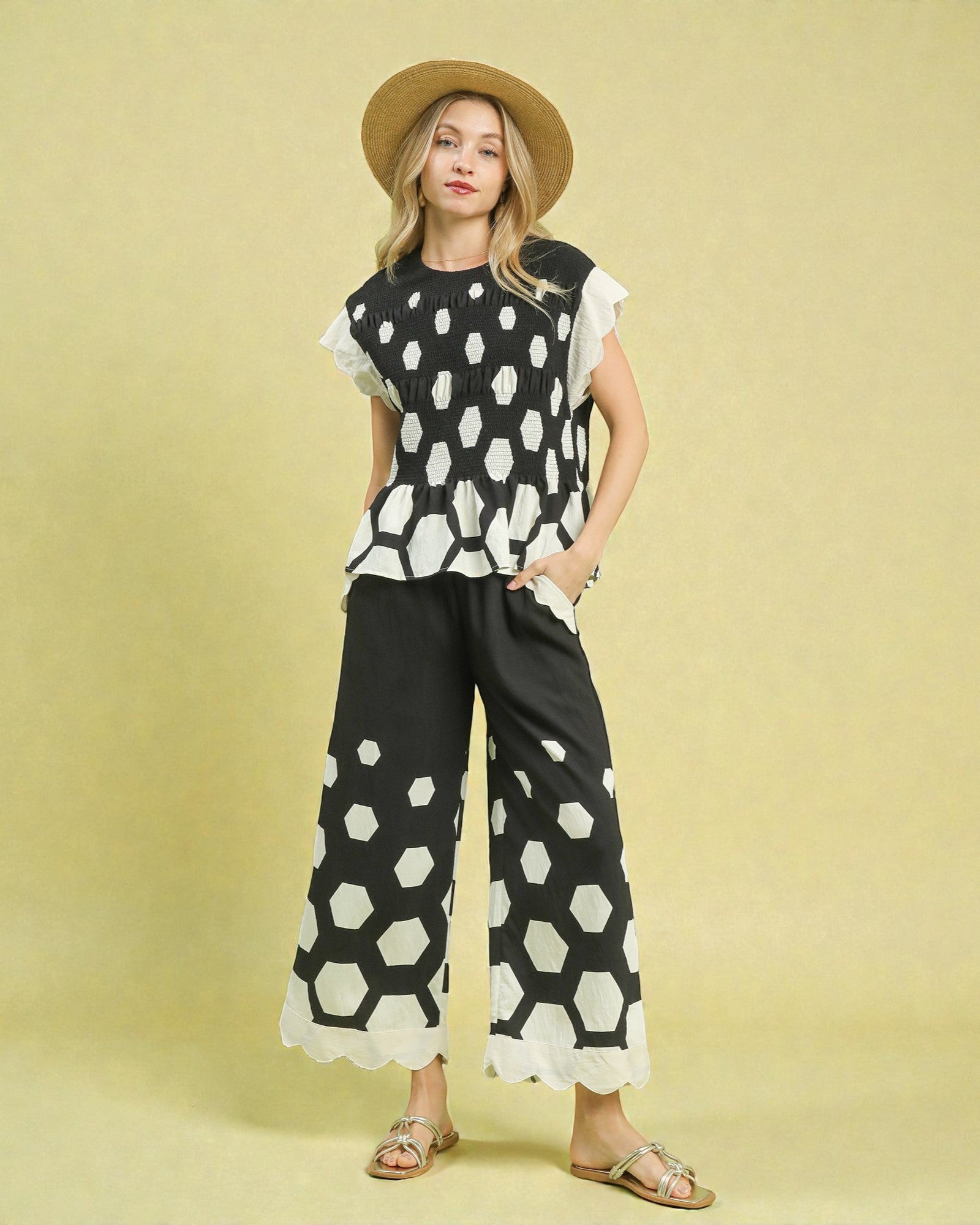 Woman wearing a black and white patterned outfit with a straw hat on a yellow background