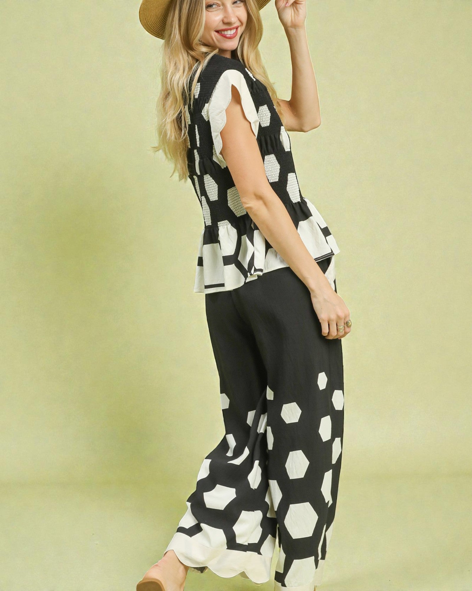 Woman wearing a black and white patterned sleeveless top and wide-leg pants on a yellow background