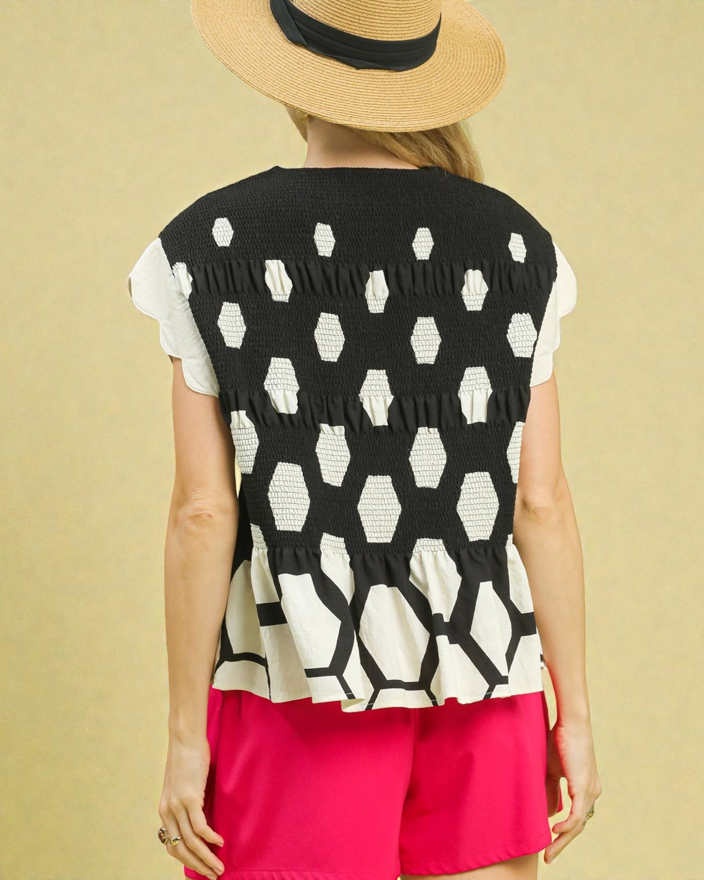 Person wearing a black and white patterned sleeveless top with pink shorts on a beige background