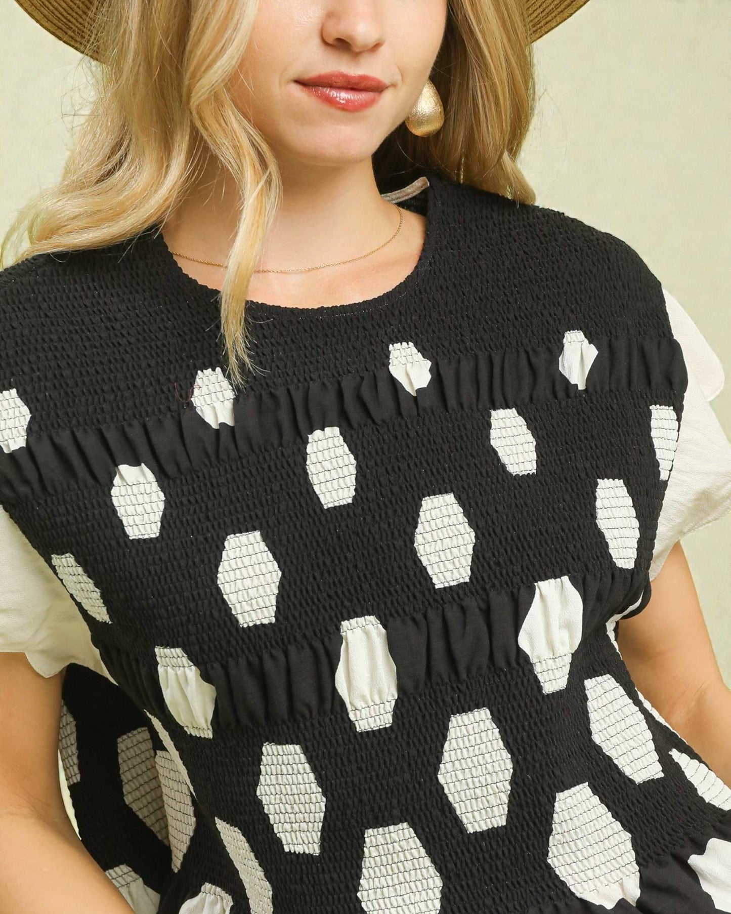 Woman wearing a black dress with white geometric pattern and straw hat.