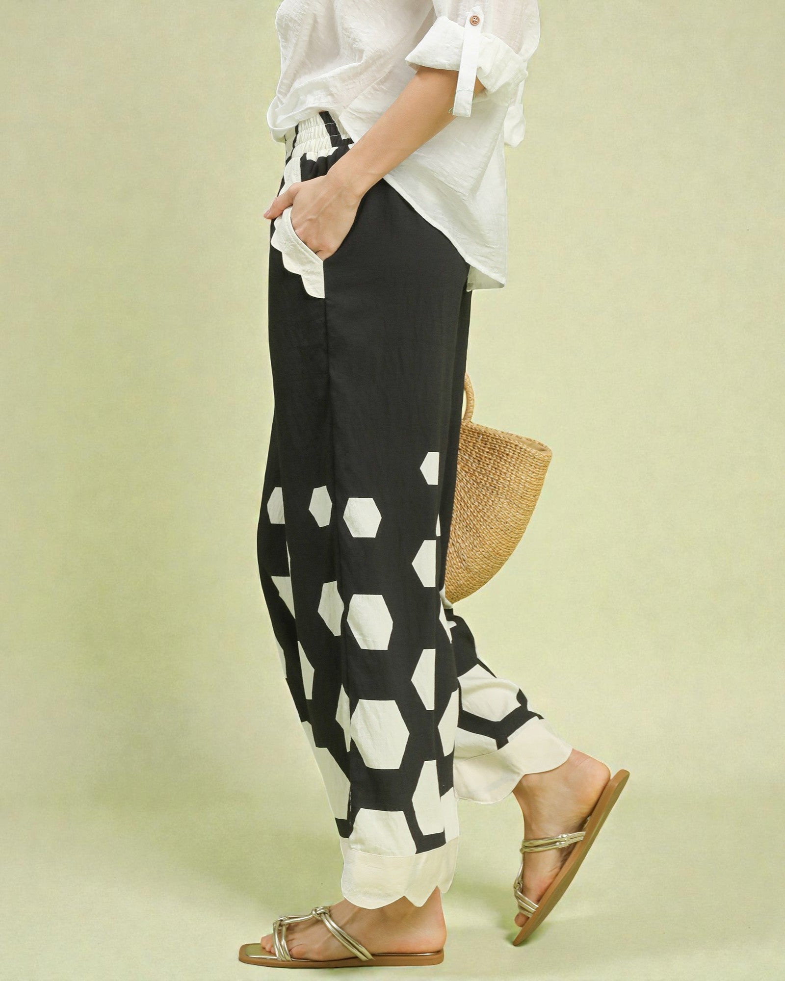 Person wearing black and white patterned pants with a white shirt on a light green background