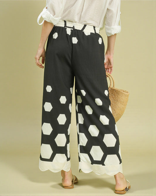 Person wearing black pants with white geometric pattern on a beige background