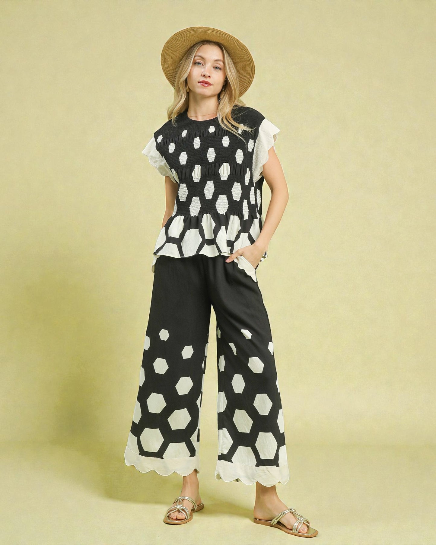 Woman wearing a black and white patterned outfit with a straw hat on a beige background