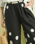 Person wearing black pants with white geometric patterns, holding a straw bag.