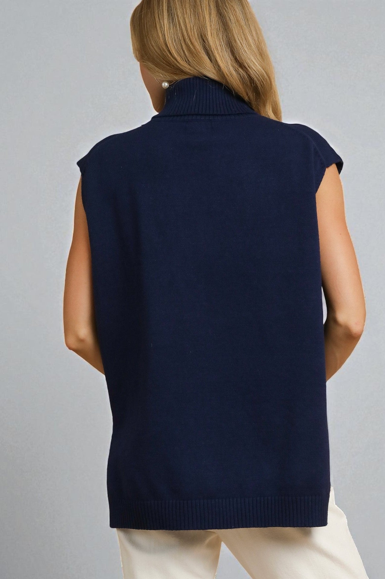 Person wearing a navy blue sleeveless sweater over a white shirt on a gray background