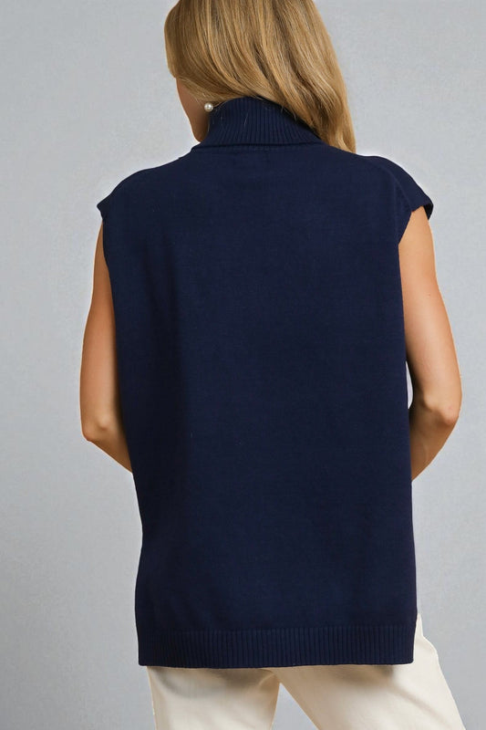 Person wearing a navy blue sleeveless sweater over a white shirt on a gray background