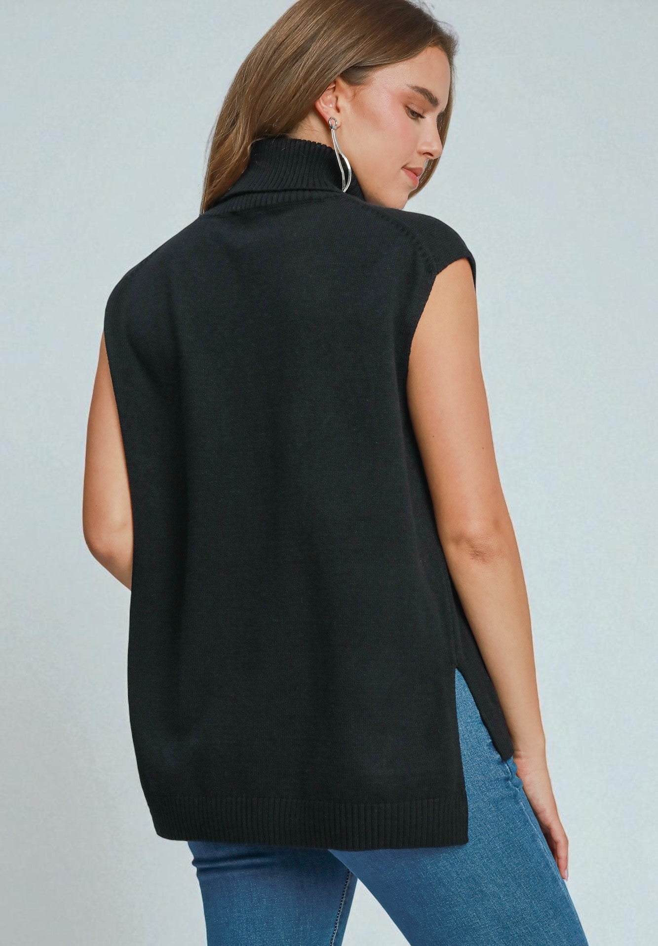 Woman wearing a black sleeveless sweater over a blue top against a light gray background