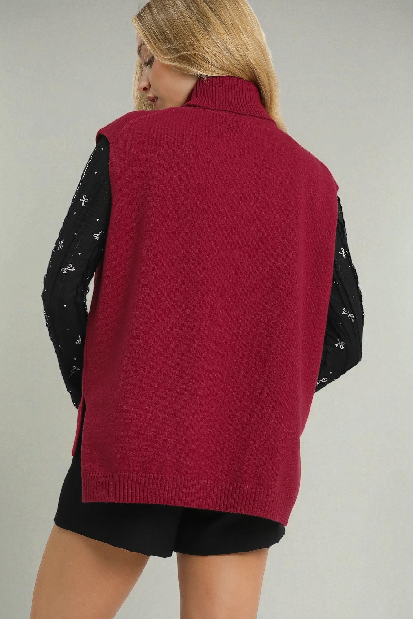 Person wearing a red vest over a black long-sleeve shirt with white patterns on a plain background