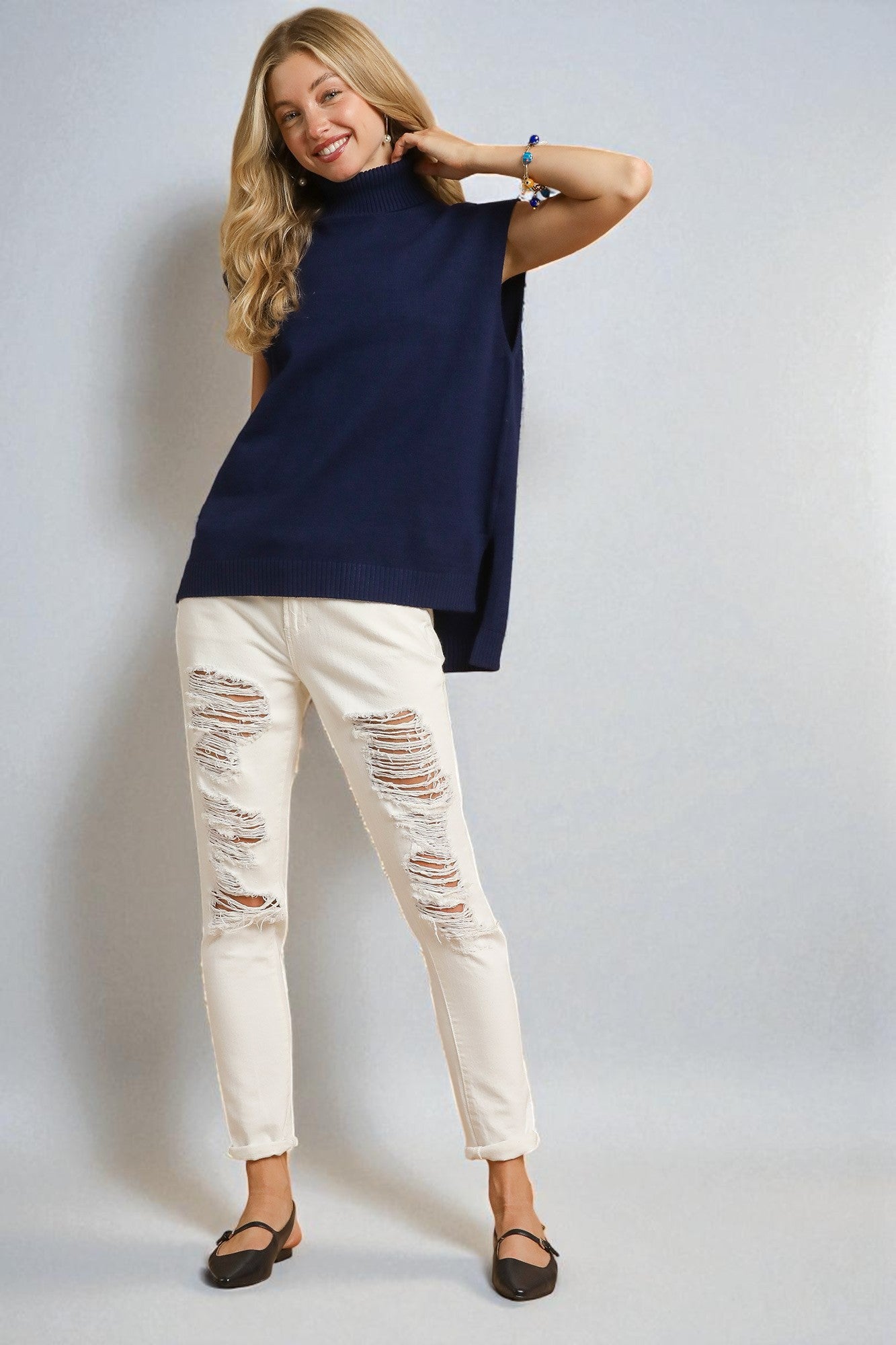 Woman wearing a navy top and white distressed jeans against a plain background