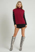 Woman wearing a red sleeveless sweater, black shorts, and gray snake print knee-high boots on a white background