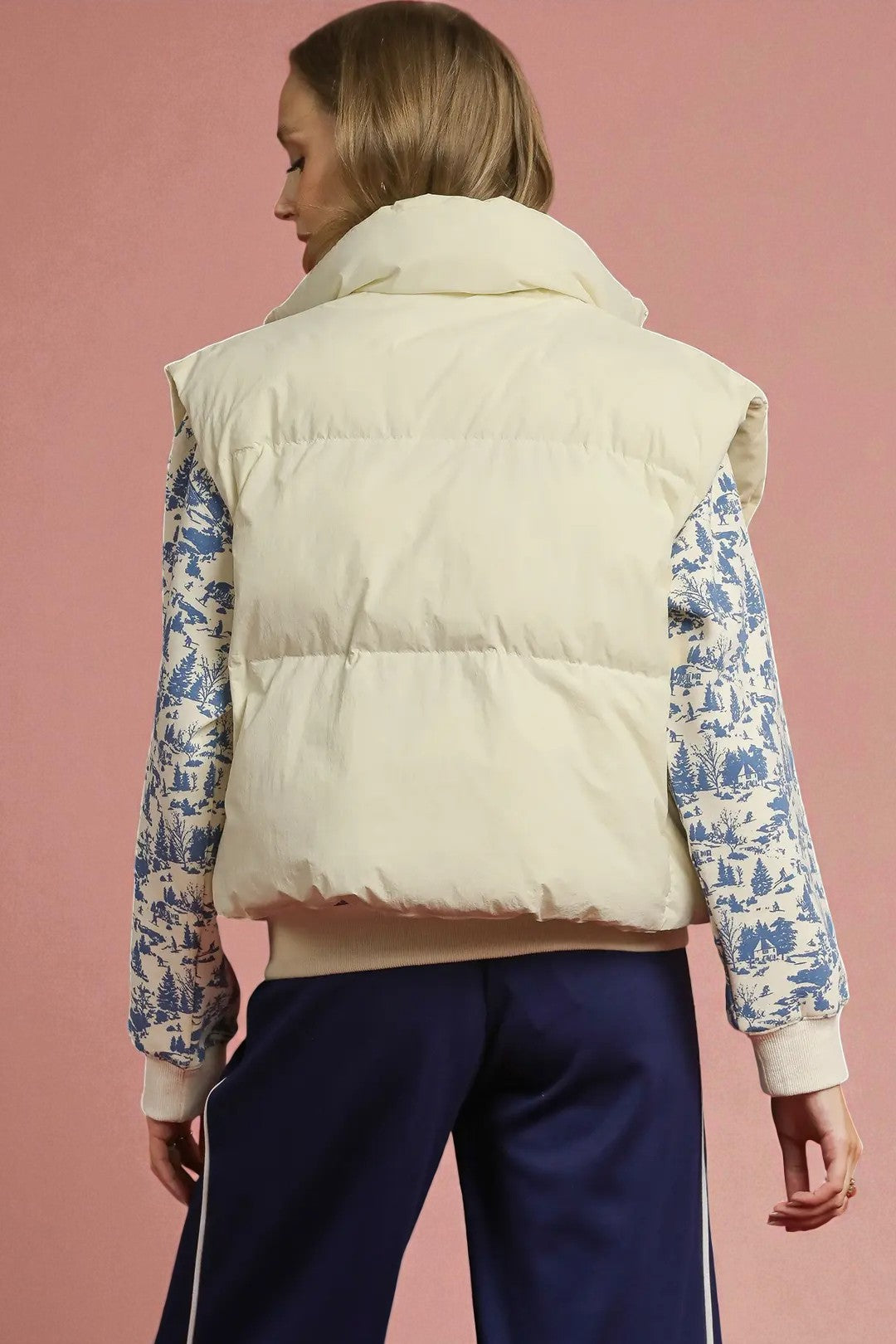 Person wearing a beige puffer vest over a patterned shirt with a pink background