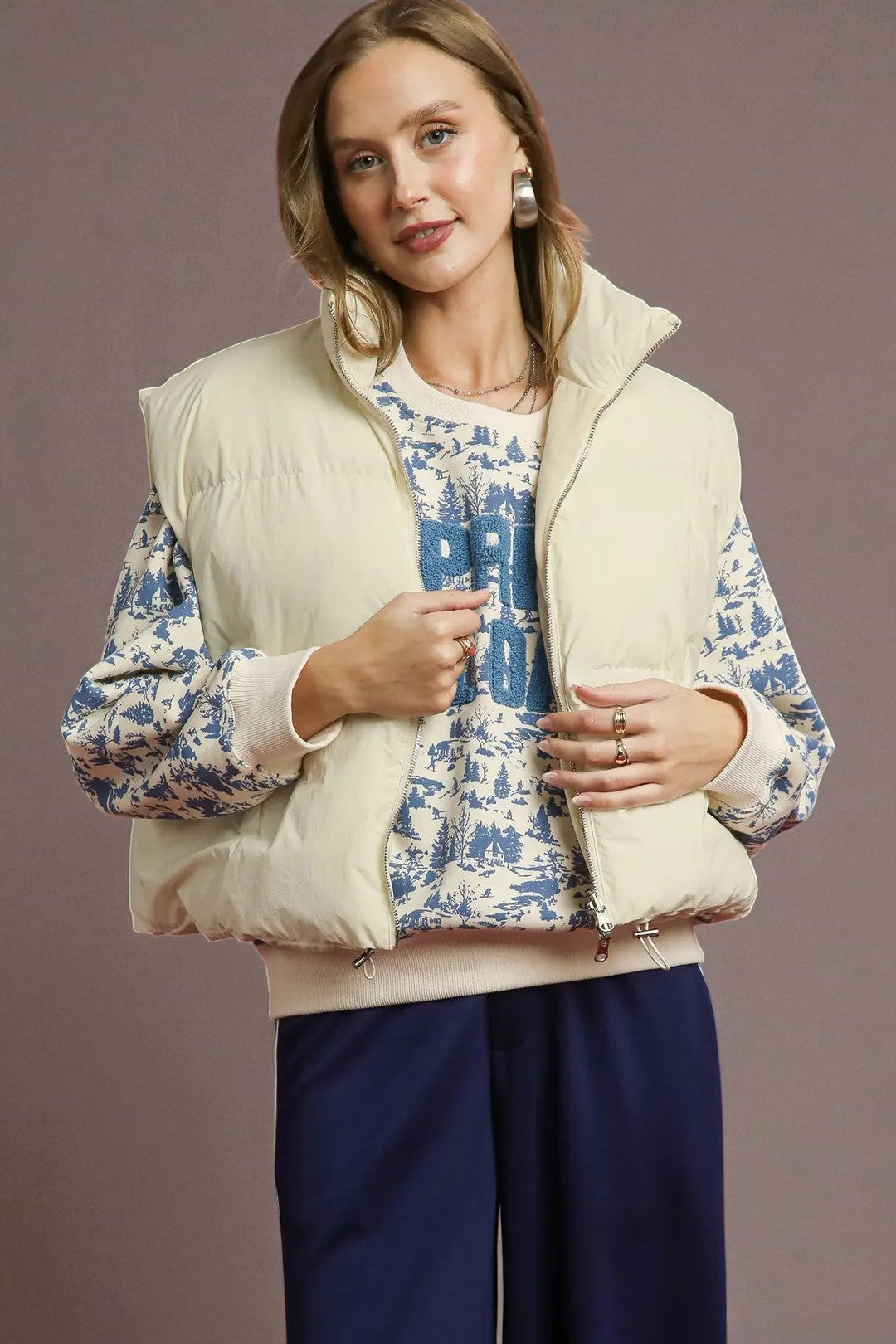 Woman wearing a cream puffer vest over a blue floral shirt with a plain background